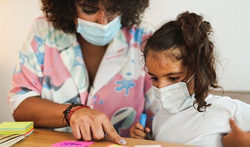 Mother doing home schooling with child while wearing surgical face mask for coronavirus