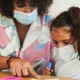 Mother doing home schooling with child while wearing surgical face mask for coronavirus