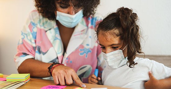 Mother doing home schooling with child while wearing surgical face mask for coronavirus